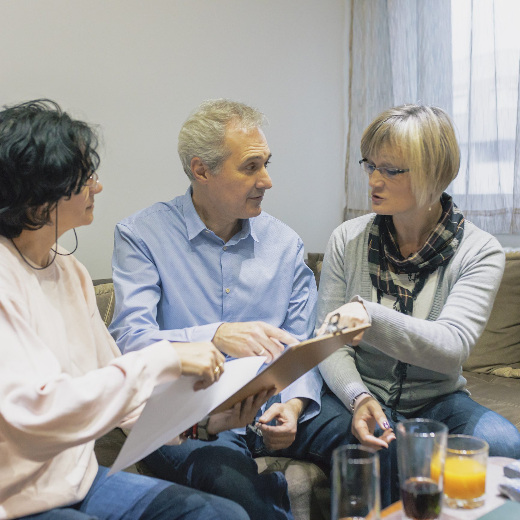 Three people discussing documents on couch.