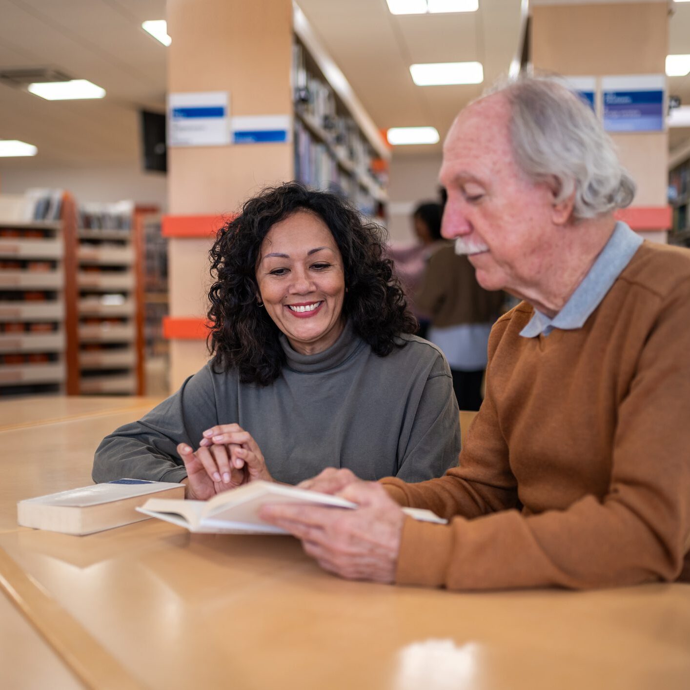 Two people reading together in a library.
